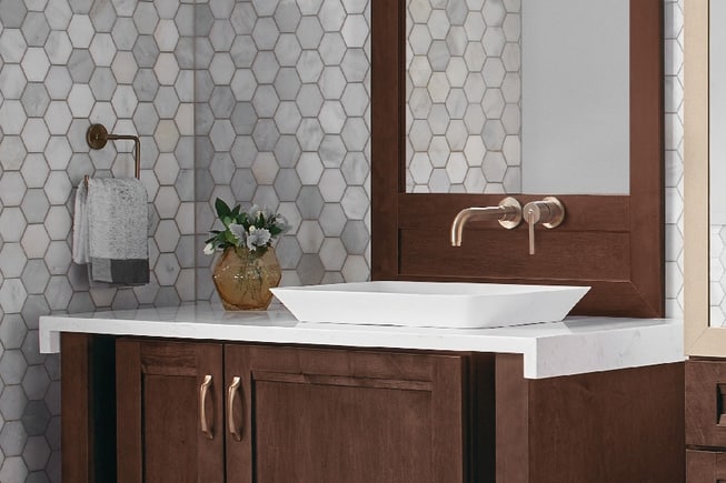 dark walnut bathroom vanity with rose gold hardware, white marble countertop, and gray hex tile walls