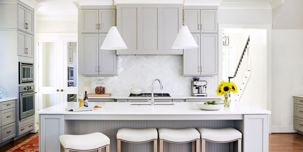 remodeled kitchen with light grey cabinets, white countertops, a rich medium wood floor, and a kitchen vent hood hidden behind faux cabinetry