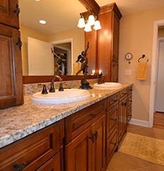 remodeled bathroom vanity with medium wood cabinets, light stone countertop, and white sink with antique bronze fixtures